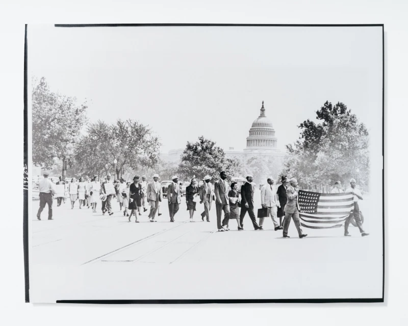 Black and white photograph of a large group of people walking on a street with the United States Capitol building in the background.
