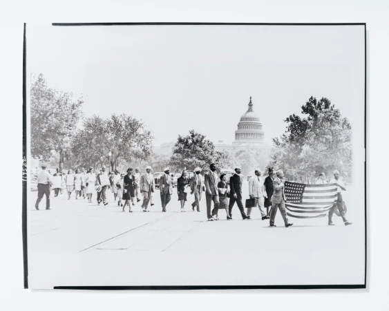 Black and white photograph of a large group of people walking on a street with the United States Capitol building in the background.
