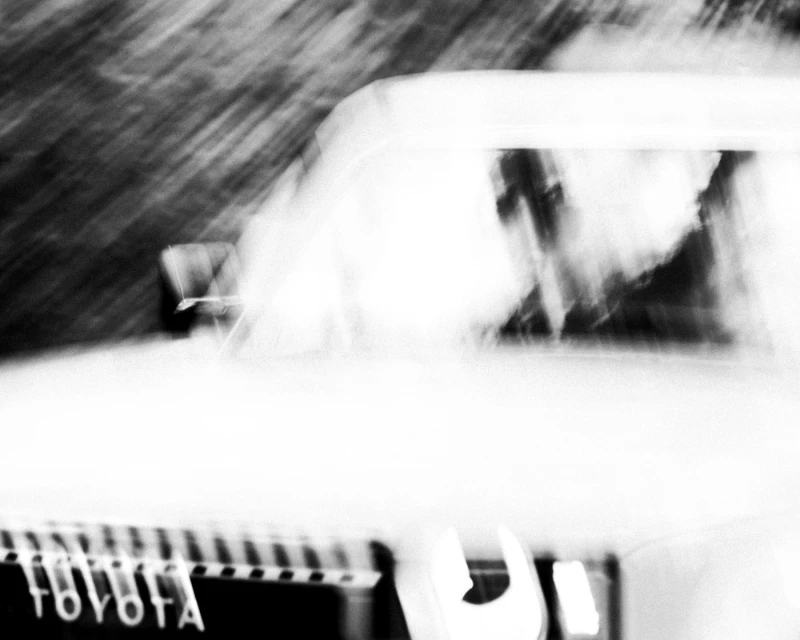 Blurred black and white image of a vintage Toyota car with a focus on motion and abstract qualities, highlighting the car's front grill.