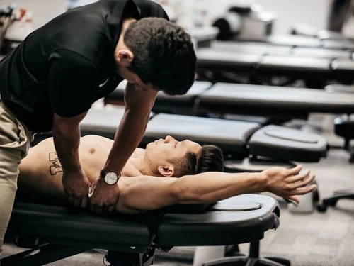 Man receiving massage therapy from another man in a clinic setting, focusing on musculoskeletal health and wellness, showcasing a health care context.