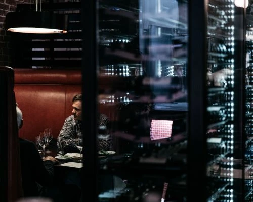 Two people seated at a table in a dimly lit restaurant with booth seating and a wine rack visible in the background.