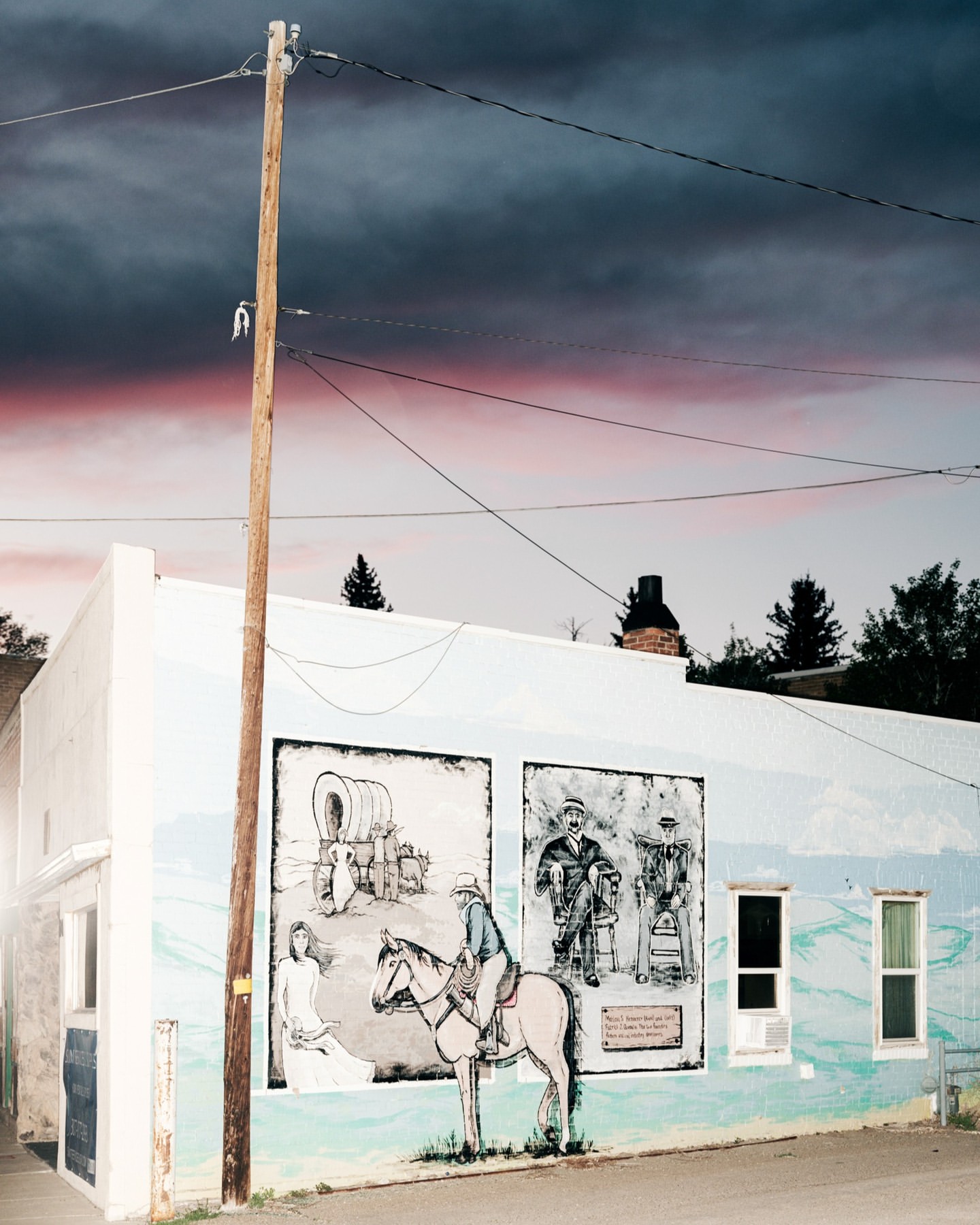 Building exterior with a mural depicting a Western scene with a woman, a horse, and figures, set against a dramatic sky at dusk.