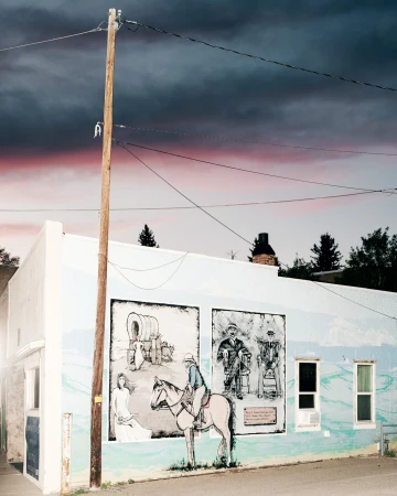 Building exterior with a mural depicting a Western scene with a woman, a horse, and figures, set against a dramatic sky at dusk.