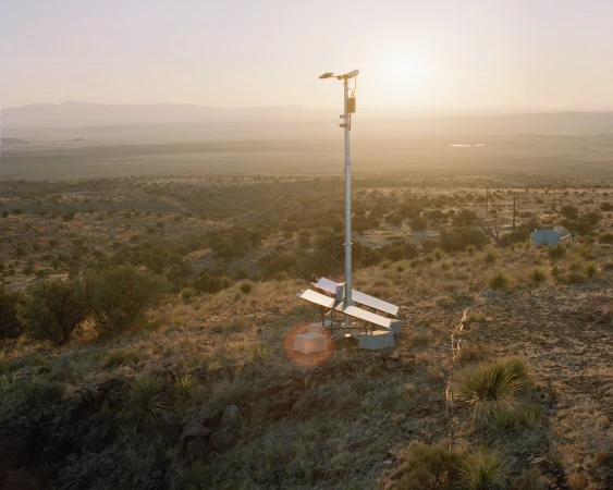 Solar panel array installation on a desert landscape, illuminated by the golden light of a setting sun, and distant mountains.