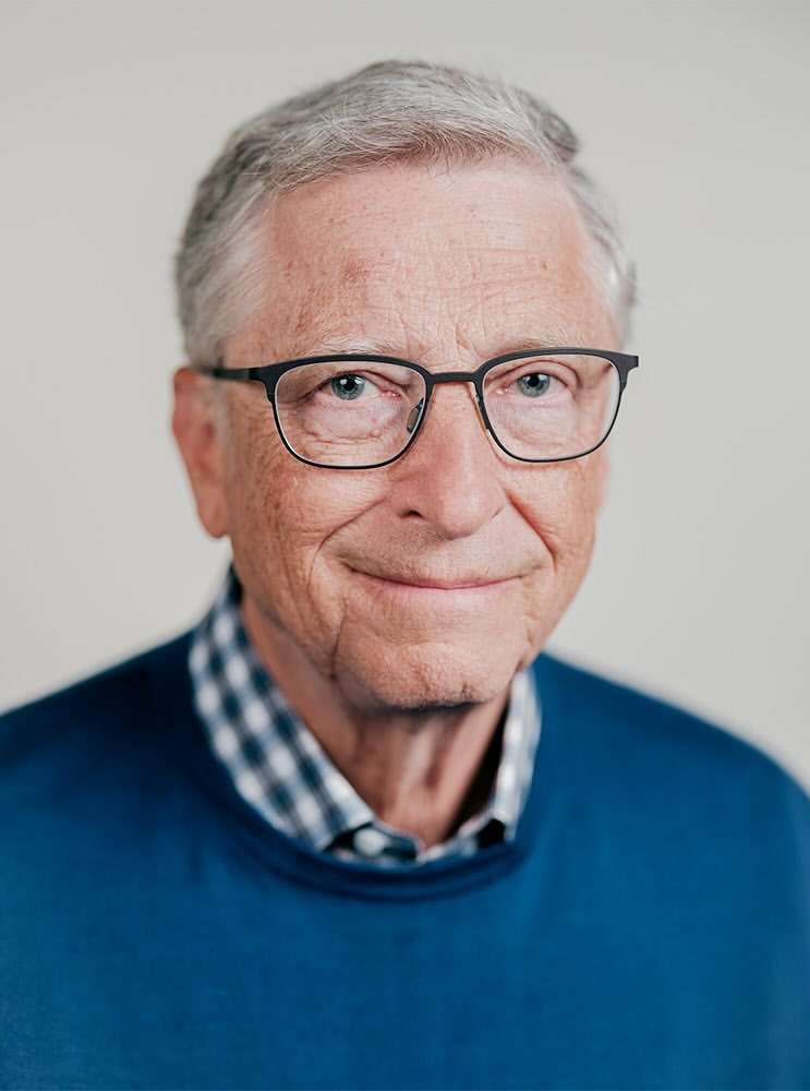 Portrait of Bill Gates wearing glasses and a blue sweater against a plain white background