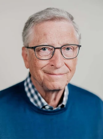 Portrait of Bill Gates wearing glasses and a blue sweater against a plain white background