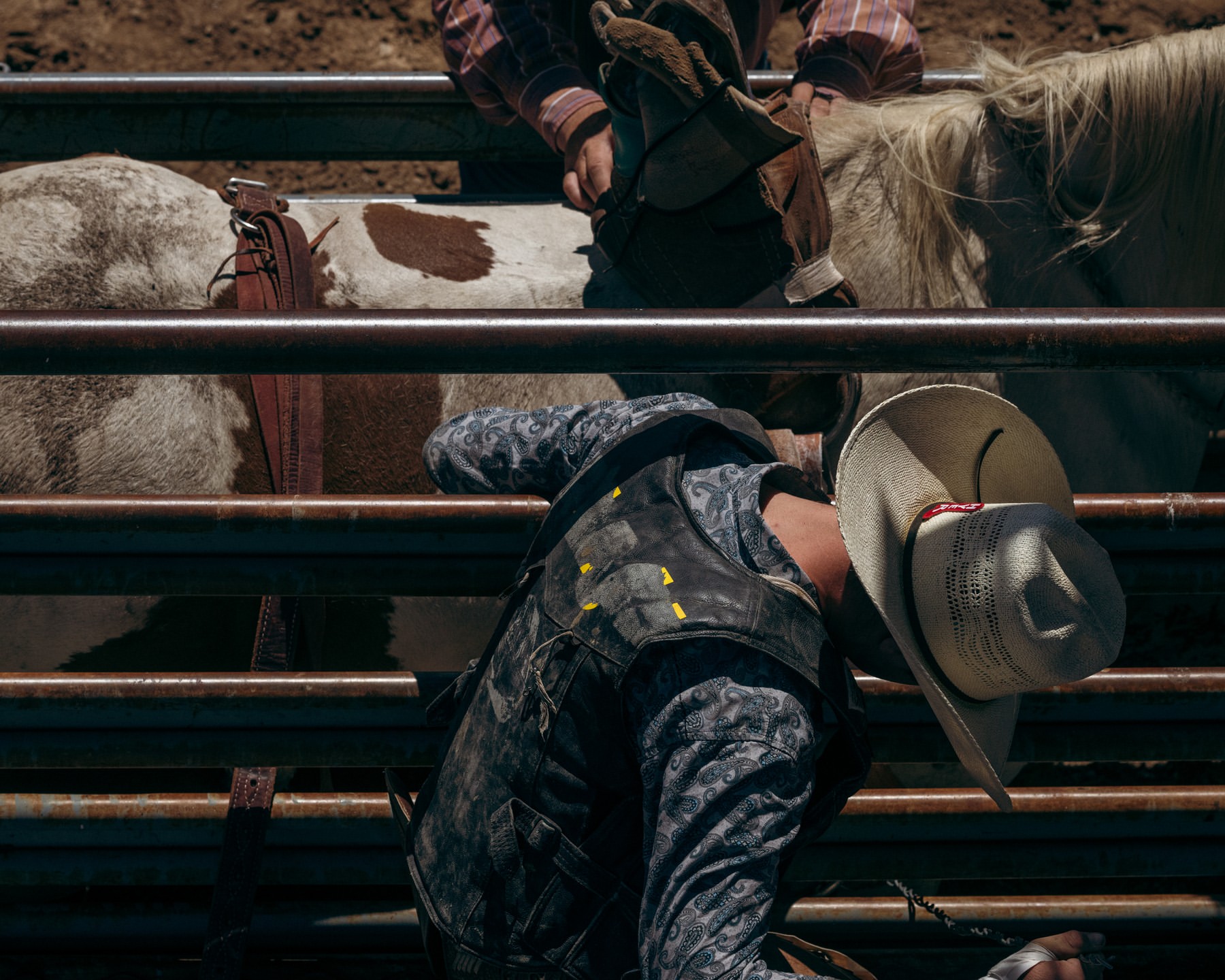 Rodeo athlete on bucking bronco in outdoor arena; the cowboy wears a hat and vest as a second cowboy looks on from behind.