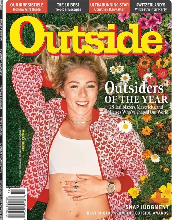 Magazine cover of Outside featuring a smiling adult woman in a patterned jacket lying in a field of grass and flowers.