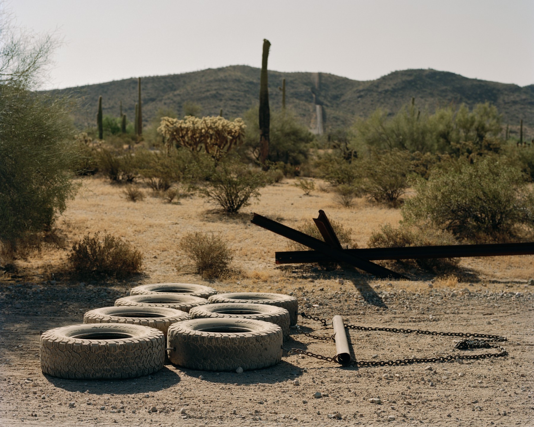 Landscape featuring a set of tires chained together in the desert near cacti and mountains on a sunny day.