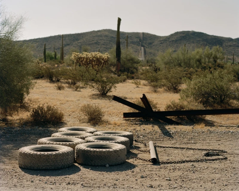 Landscape featuring a set of tires chained together in the desert near cacti and mountains on a sunny day.