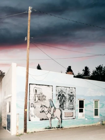 Outdoor mural depicting historical figures and scenes painted on the side of a white building with a telephone pole and cloudy sky.