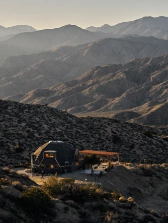 Exterior view of a modern home nestled in a mountainous desert landscape, illuminated by soft sunlight, showcasing architecture and environment.