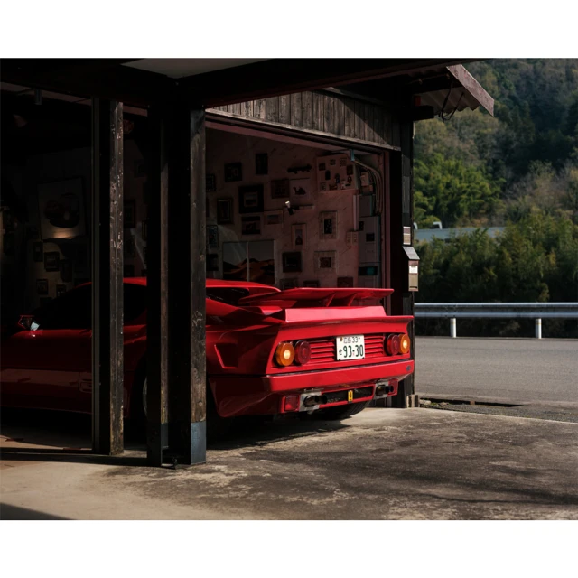 Rear view of a red Ferrari parked inside of a garage, with a view of a lush, green landscape during daytime.
