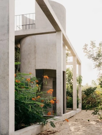Exterior view of modern architectural concrete building with tropical plants and surrounding trees against an overcast sky.