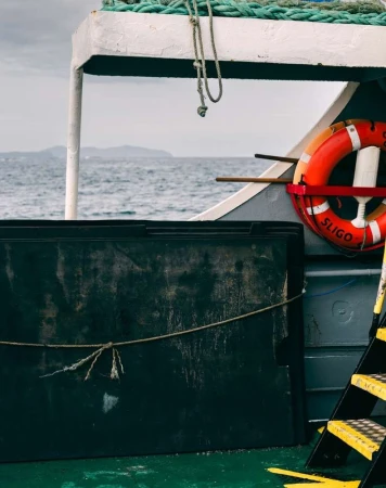 Marine scene featuring a black box on a ship deck, with a life preserver, sea, and distant land visible in the background.