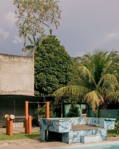 Outdoor scene showcasing a cyan bench near a swimming pool, complemented by lush green vegetation, creating a serene and tropical ambiance.