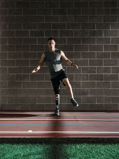 Man with prosthetic leg balances on indoor track, demonstrating fitness and determination against a grey brick wall backdrop.