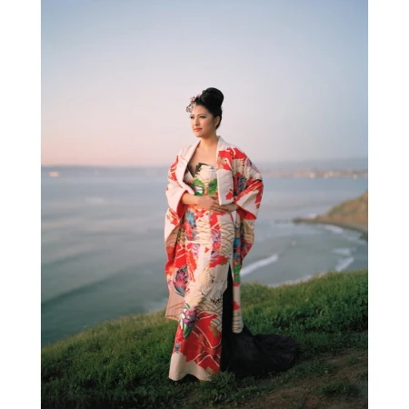 Woman in colorful kimono stands on a grassy hill overlooking the ocean at dusk, showcasing traditional Japanese fashion and natural beauty.