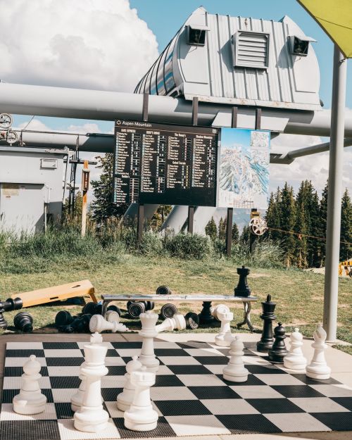 Outdoor chessboard set at Aspen Mountain resort with cable car infrastructure and scenic mountain backdrop on a bright day.