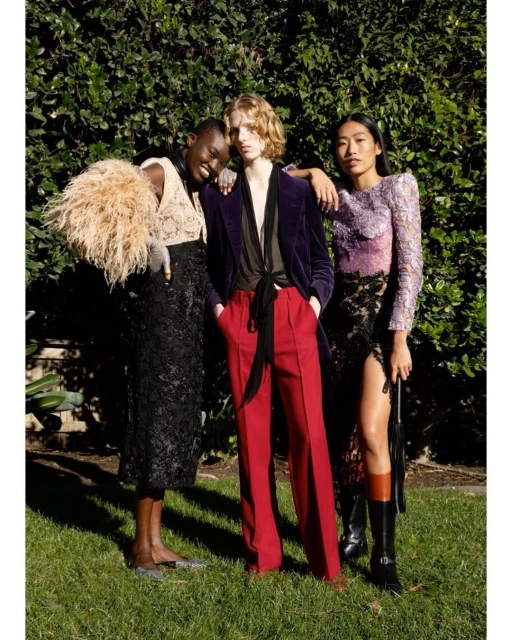 Three diverse fashion models pose together in an outdoor setting with lush green foliage, showcasing stylish eveningwear and textures.