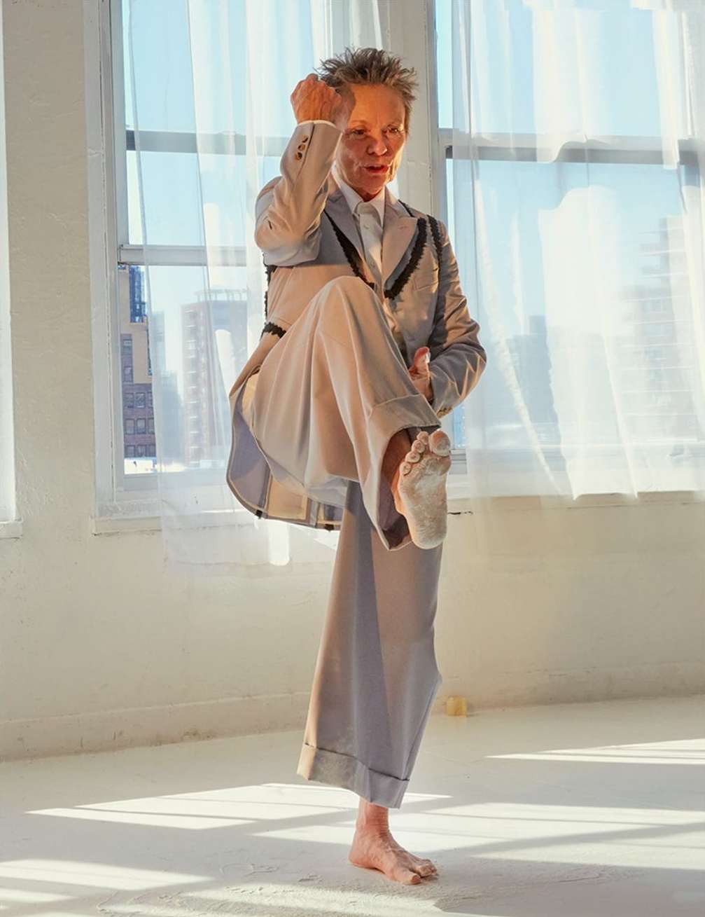 Person in a light gray suit practices martial arts barefoot in a light-filled interior space. Tall windows filter sunlight.