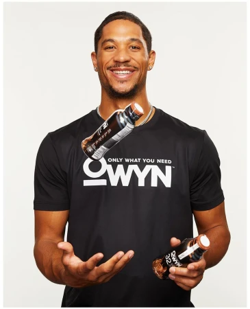 Smiling black man wearing a black OWYN t-shirt with two beverage bottles floating against a white background