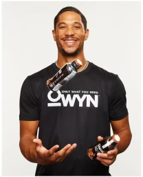 Smiling black man wearing a black OWYN t-shirt with two beverage bottles floating against a white background