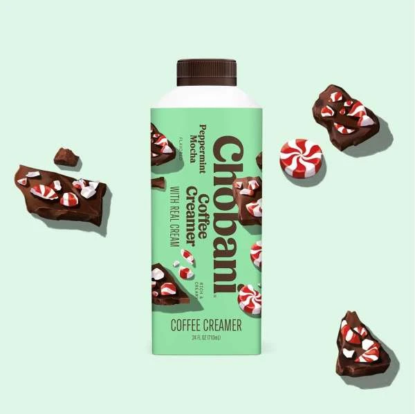 Chobani Peppermint Mocha Coffee Creamer bottle on a light green background with pieces of chocolate bark and peppermint candies.