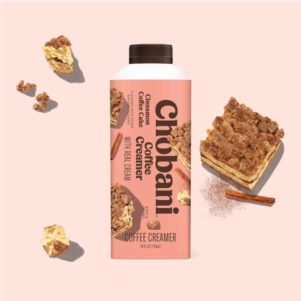Chobani cinnamon coffee cake flavored coffee creamer in a plastic bottle with slices of coffee cake on a pink background.