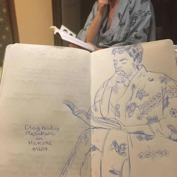 Sketch of a man in a robe reading, inside a notebook, with a person in a robe in the background reading a script or book.