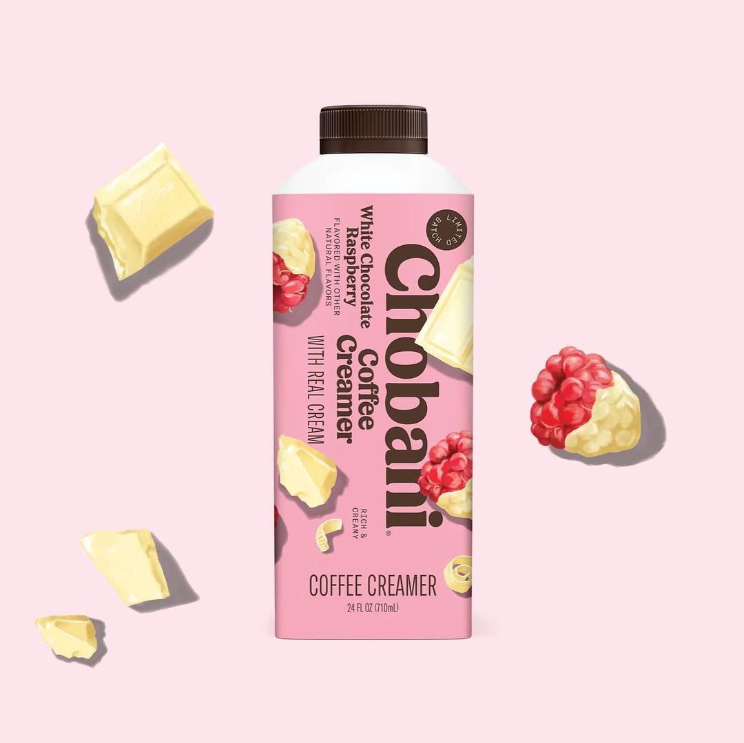 Chobani White Chocolate Raspberry coffee creamer bottle on pink background with white chocolate and raspberries scattered around.
