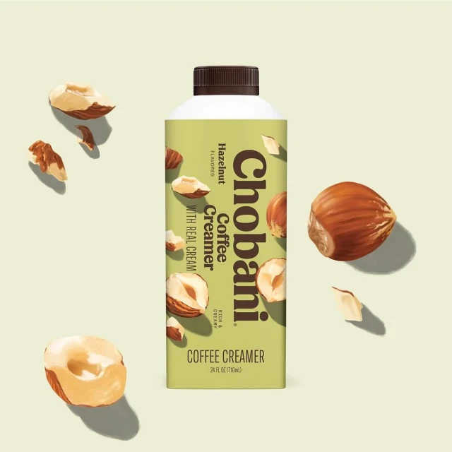 Chobani Hazelnut flavored coffee creamer in a carton with scattered hazelnuts against a light background. Food and beverage concept.