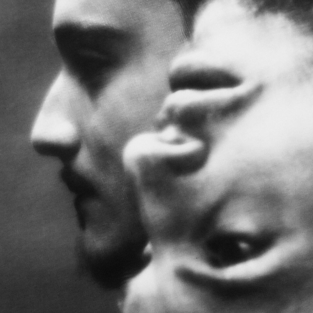 Black and white portrait featuring the face of one adult male with another slightly out of focus in the background, artistic presentation.