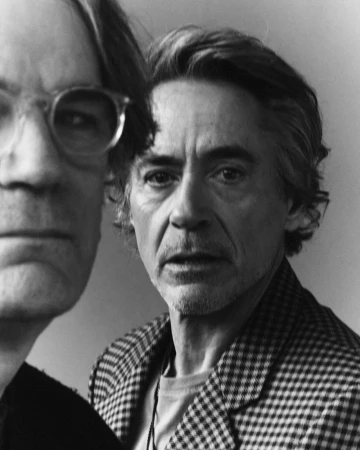 Black and white portrait of Robert Downey Jr. in a patterned blazer alongside another man wearing glasses.