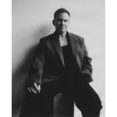 Monochrome portrait of a man in his 50s wearing a dark blazer seated against a plain light wall