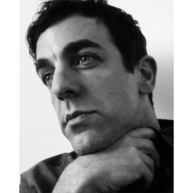 Monochrome portrait of a contemplative man with dark hair, resting his chin on his hand, set against a simple, light background.
