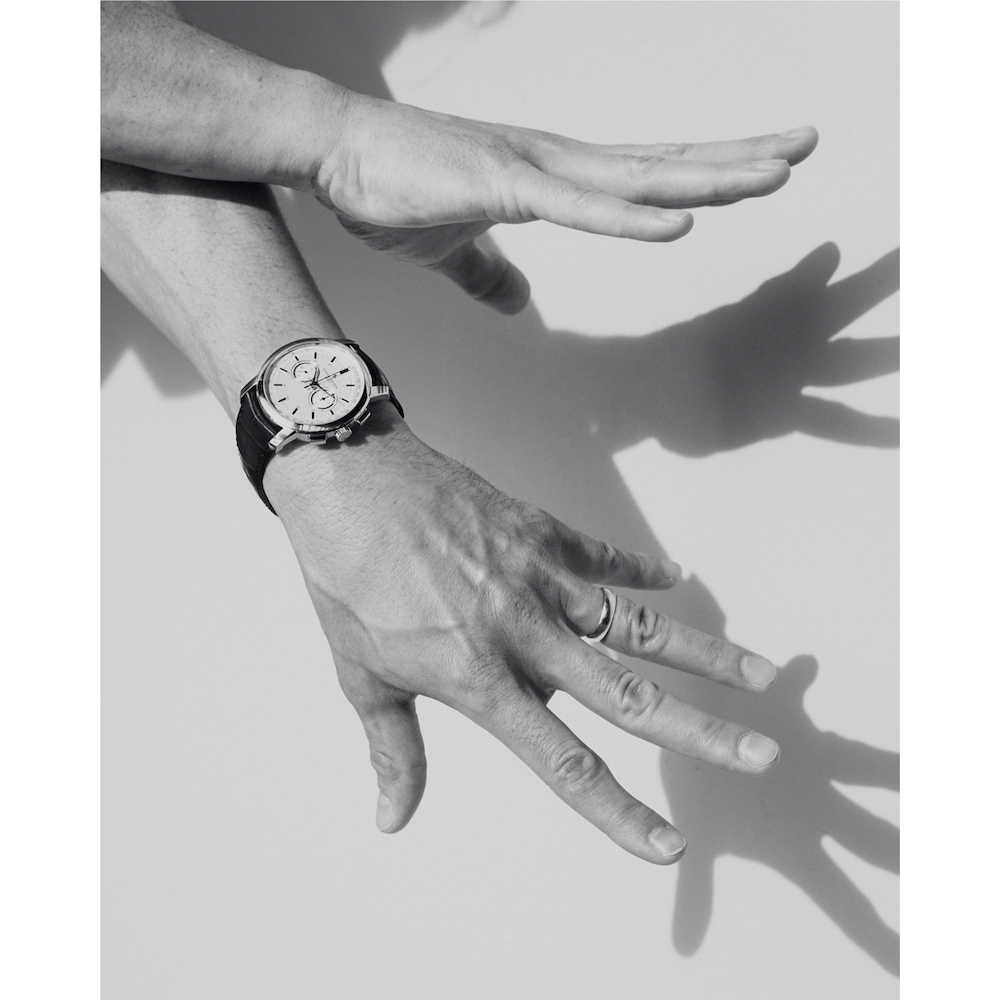 Close-up black and white shot of hands wearing a chronograph watch and ring against a plain background