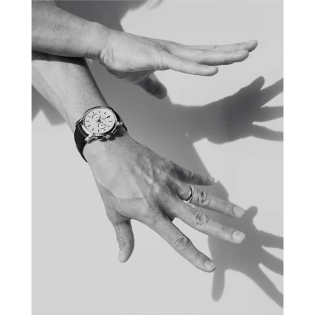 Close-up black and white shot of hands wearing a chronograph watch and ring against a plain background