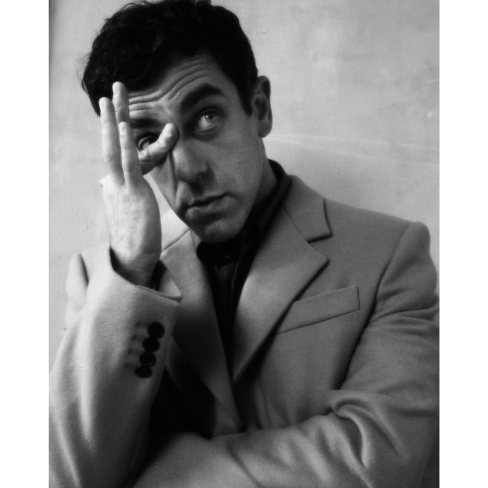 Portrait of a man in a structured suit holding fingers near his eye, photographed by Erik Tanner