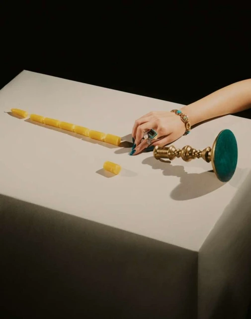 Overhead shot of a table with a woman's hand, jewelry, a segmented candle, and a brass candle holder against a dark background.