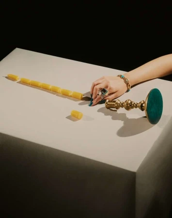 Overhead shot of a table with a woman's hand, jewelry, a segmented candle, and a brass candle holder against a dark background.