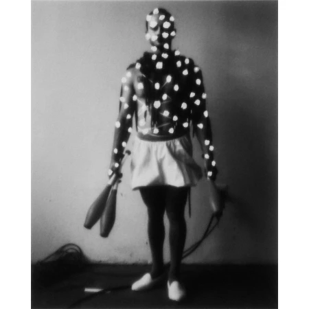 Full body shot of male circus performer covered in motion capture dots, holding juggling clubs, monochrome indoor setting.
