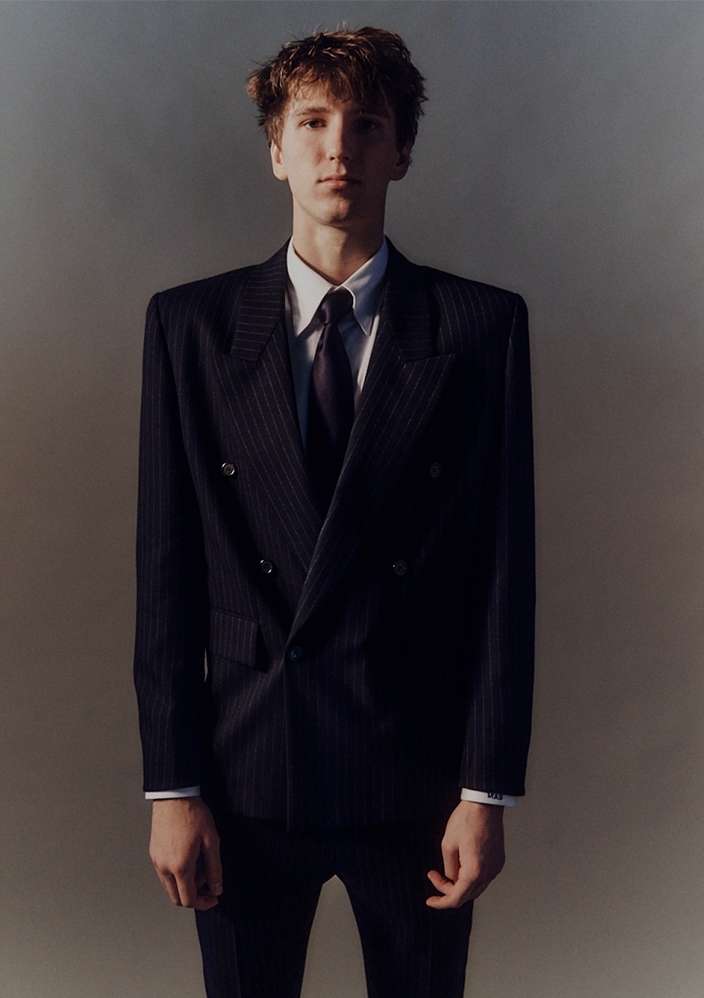 Young man in a dark pinstripe suit and tie standing against a plain gradient background captured by Erik Tanner.
