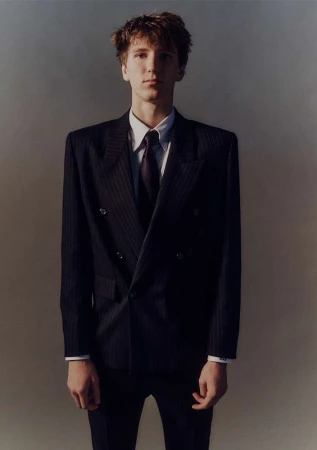 Young man in a dark pinstripe suit and tie standing against a plain gradient background captured by Erik Tanner.