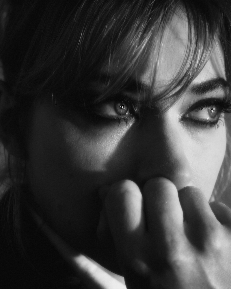 Black and white close-up portrait of an adult woman with her fingers near her mouth, looking thoughtfully into the distance.