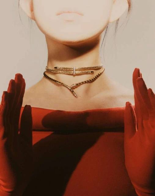 A person wearing a red strapless top and golden choker necklaces with hands raised in a studio shot, jewelry and fashion concept.
