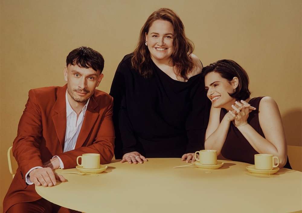 Group portrait of three people sitting at a round table indoors, with teacups and saucers in a warm, inviting ambiance.