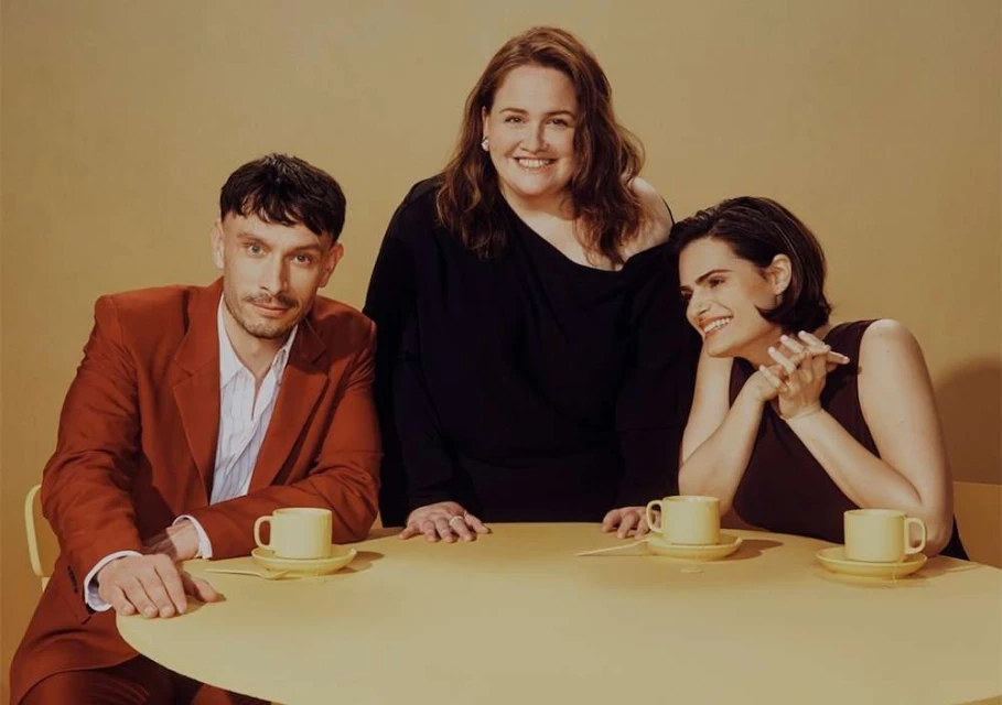 Group portrait of three people sitting at a round table indoors, with teacups and saucers in a warm, inviting ambiance.