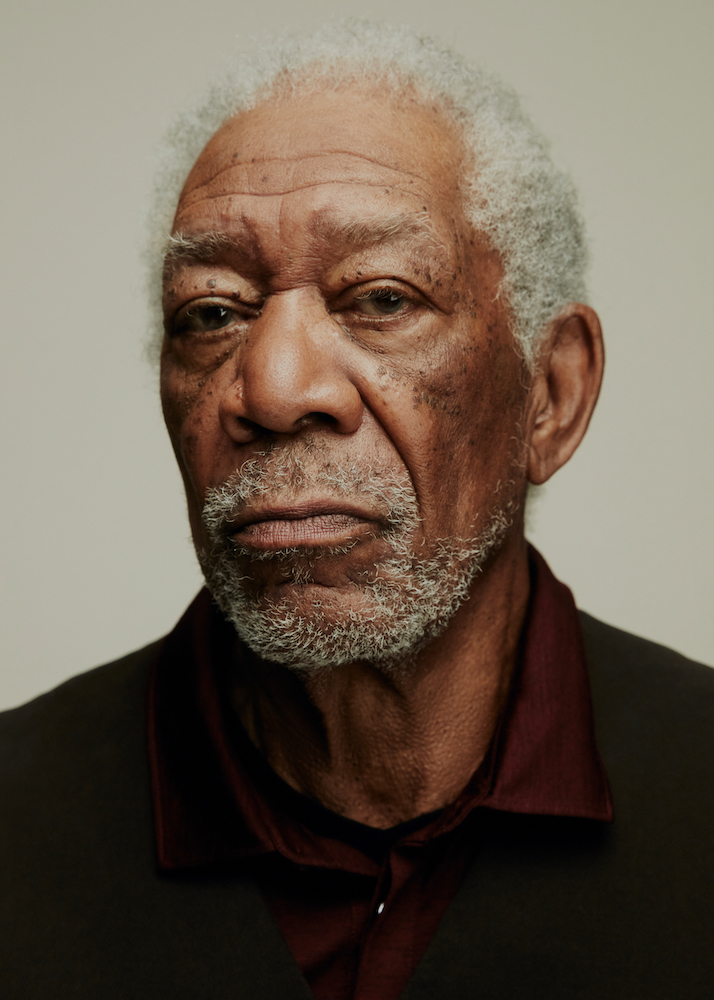 Close-up portrait of an elderly African-American man with gray hair, wearing a dark vest and maroon shirt, against a light background.