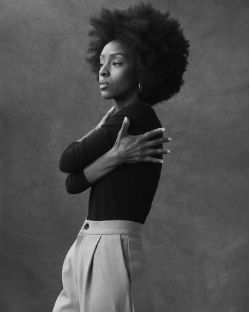 Black and white portrait of a black woman with an afro hairstyle wearing a dark fitted long-sleeve top and trousers